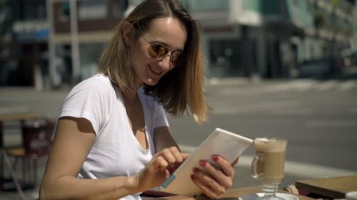 Happy Woman Using Tablet Computer and Drinking Coffee in Cafe in City 30s