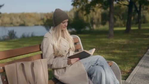 Blonde Woman in Hat Reads Book Happy on Park Bench in Autumn
