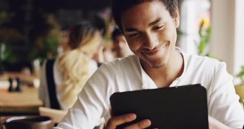 4k video footage of a handsome young man sitting in a cafe and using a digital tablet