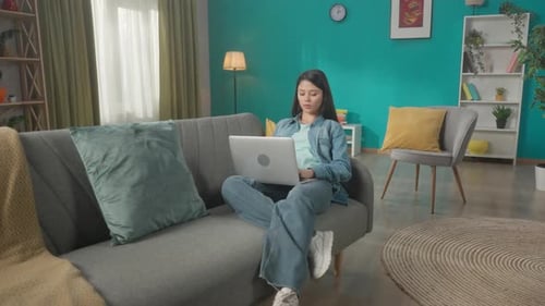 Young Woman Using Laptop on Couch at Home