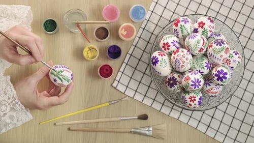 Female hands painting with paints and brush on an Easter eggs