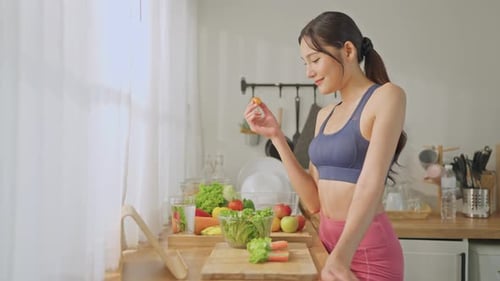 Asian attractive sportswoman eatting green salad in kitchen at home.