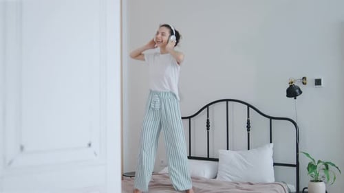 Woman Dancing on Bed with Headphones in Bedroom