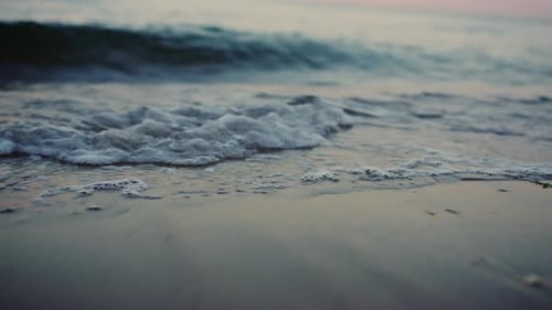 Sea waves splashing sand beach on coastline in slow motion at twilight dawn