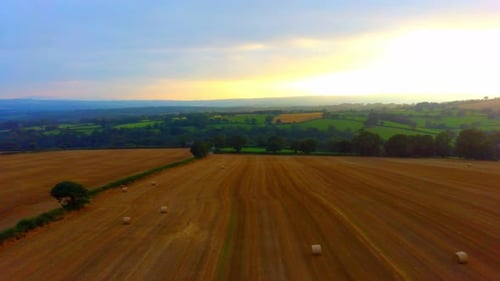 Backward movement with lovely view of a yellow field with hay bales and a sunset.