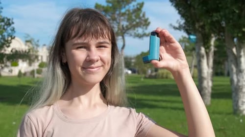 Teen Holds Inhaler in Park on Sunny Day