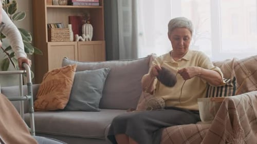 Caregiver Assisting Aged Woman with Walkers while Others Resting in Nursing Home