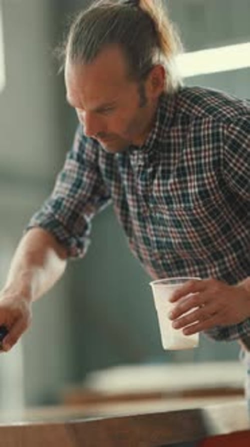 Focused Man Painting Wooden Surface with Roller in Workshop