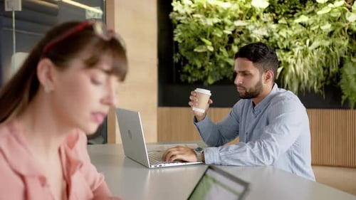 Travaillant au bureau, homme utilisant un ordinateur portable et tenant une tasse à café, femme utilisant une tablette