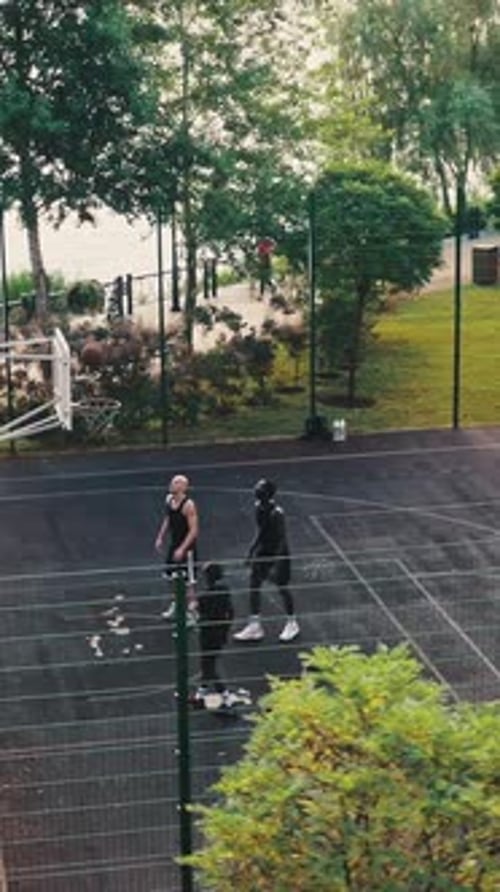 Schöne Aussicht von oben auf den von Bäumen umgebenen Basketballplatz der Stadt Ein Team von Jungs spielt ein Freundschaftsspiel