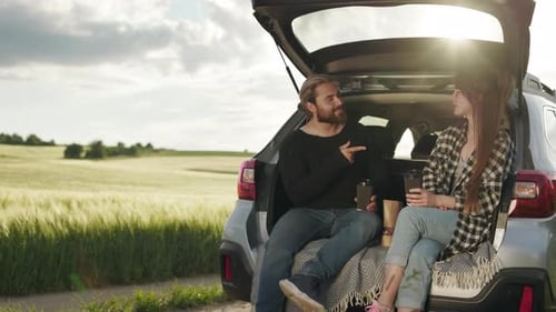 Couple Talking and Smiling in Open Car Trunk at Green Field