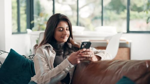 Woman Relaxing on Couch Uses Smartphone Indoors
