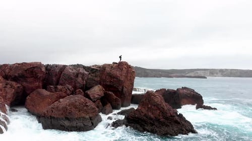 AERIAL: A guy standing the cliff revealing a beautifull coastline