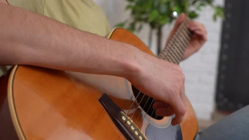Adult Man Guitarist Sitting in the Room Playing Acoustic Guitar Fingering Strings Chords Close Up