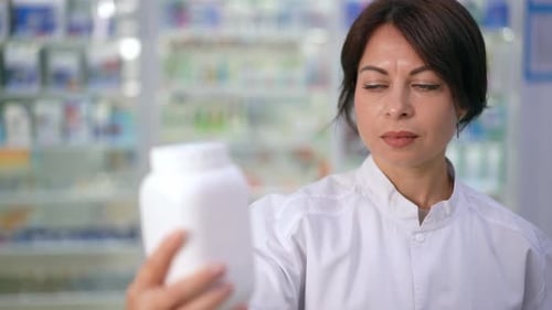 Woman in Lab Coat Examining Medicine Bottle