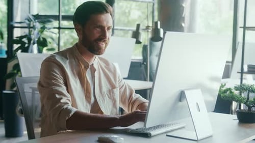 Smiling Man Working at Modern Office Desk with Desktop Computer