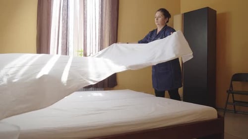 Female Housekeeper Changing Bedding in a Hotel Room