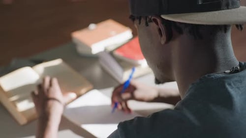 Behind View Man Taking Notes From Book in Library