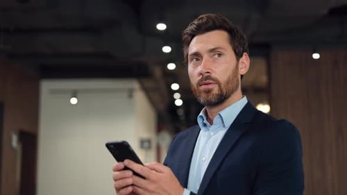 Handsome Businessman in Suit Chatting Online on Modern Smartphone in Office
