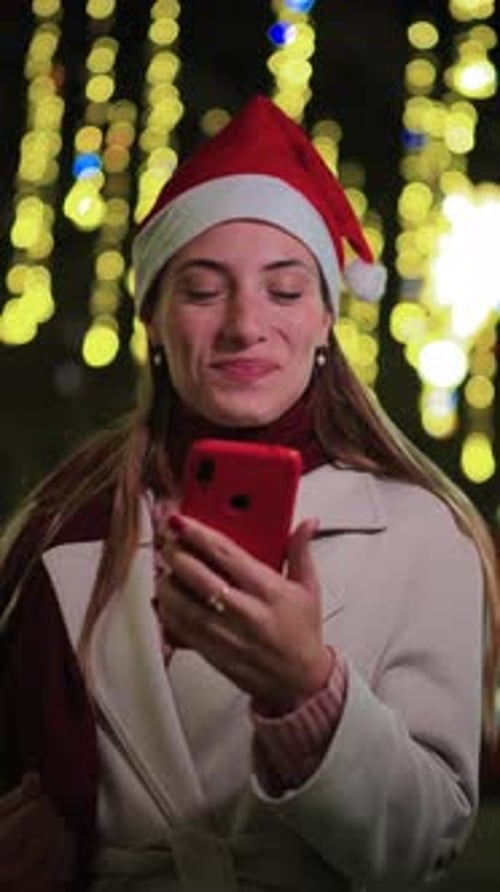 Smiling Woman in Santa Hat Using Smartphone at Night