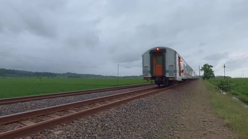 Bahngleise durch grüne Landschaft mit fahrendem Zug