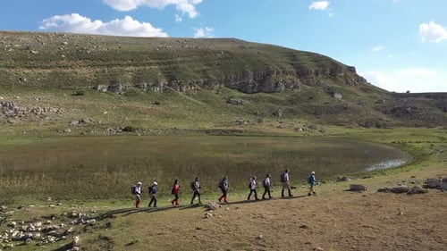 Aerial View Of Group Of People Hiking By The Pond On The Mountain Slope