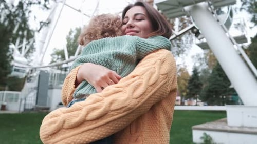 Loving mother walks with her cute daughter in the park in sweaters. She holds her daughter in her ar