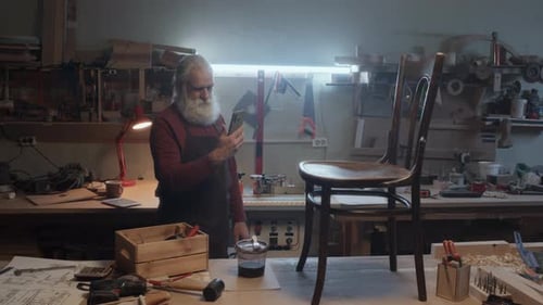 Artisan Stands With Mobile Phone In Woodworking Shop