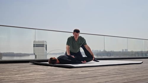Man Stretching Partner's Leg Outdoors on Sunny Day