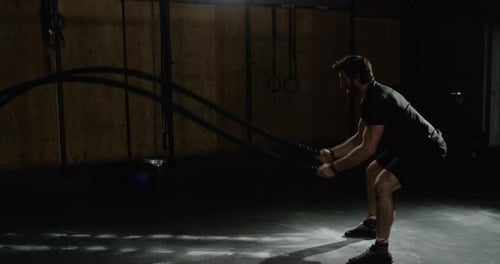Man Exercising with Battle Ropes in Dark Gym