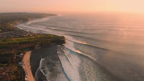 Surfing ocean waves at warm sunset in Bali. Aerial view of coastline and beach with big waves.