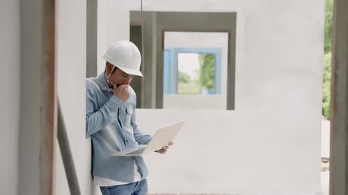 Indian architect with a mustache leaning against the cement wall of an unfinished house Carefully ex