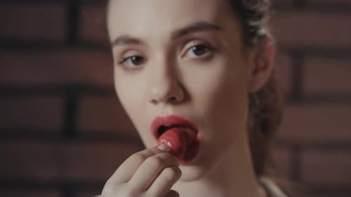 Glamorous Woman Eating a Strawberry in Front of Brickwall