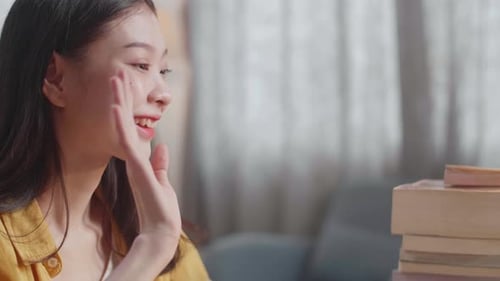 Close Up Of Young Asian Female Waving Hand For Greeting While Studying On A Laptop At Home