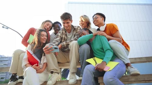 Group of Real Young People Having Fun Together with a Cellphone Siting on a Bench at University
