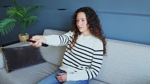 Woman Sitting on Couch Using TV Remote
