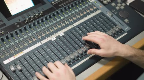 Audio Operator Adjusting Sound Levels on Faders in Professional Broadcast Control Room