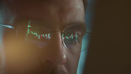 Trader Wearing Glasses is Working on Laptop Computer Screen with Stock Market Charts and Bitcoin BTC