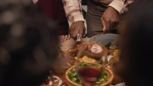 Man Serving Baked Turkey during Thanksgiving Dinner with Friends