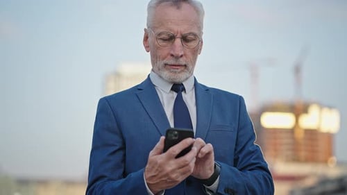 Serious Businessman Types Message to Partner on Smartphone