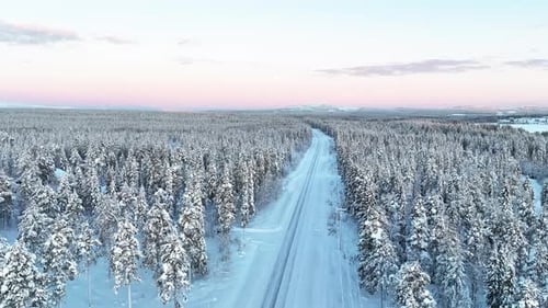 Road Through Snowy Pine Tree Forest During Winter In Finland. - aerial shot