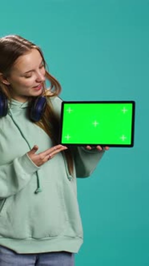 Vídeo vertical: Una joven radiante que ofrece comentarios sobre una tableta con pantalla verde