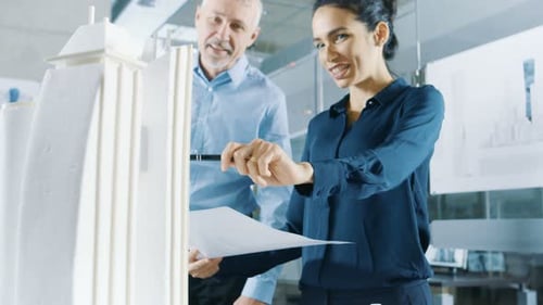 Two Professional Male and Female Architectural Engineers Work with Blueprints and on a Building Mod