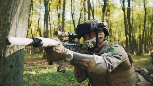 Shot of Young Soldier in Camouflage Clothes and Balaclava Holding Gun in Hands and Aiming Target