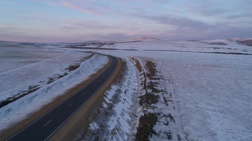 Aerial Shot of an Intercity Road with a Driving Truck Surrounded with Snow Covered Fields at Sunset