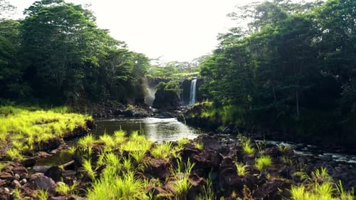 Wide rainforest river leading to tall waterfall surrounded by lush green cliffs