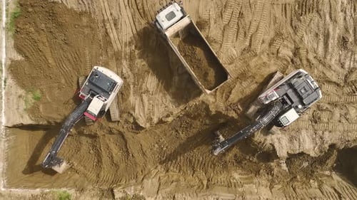 Digging Deep Aerial of Excavator and Trucks on Site