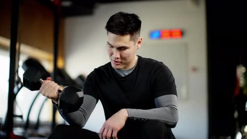A Man Holds a Dumbbell in His Right Hand and Lifts It Up and Down Slow Motion Man Sitting in Gym