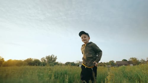 A Happy Boy Runs Across a Green Field on the Grass