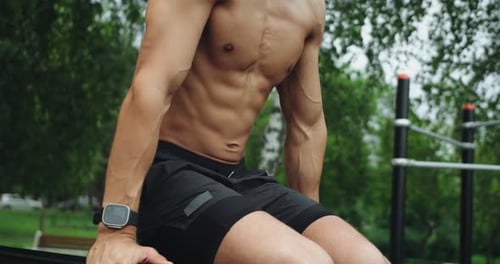 Athletic man training on parallel bar and doing abs exercise outdoors